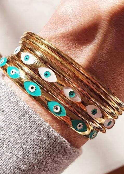 Ajoutez une touche bohème et protectrice à votre look avec ce jonc doré, élégant et symbolique. Confectionné en acier inoxydable, il est orné de 7 œillets protecteurs sur la face avant, chacun représentant un symbole d'œil grec pour éloigner les énergies négatives et attirer la protection.